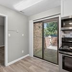 Bright and modern kitchen with sleek appliances, wood-style flooring, and a sliding glass door opening to a charming brick patio.