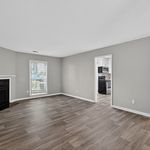 Inviting living room featuring modern hardwood flooring, ample natural light from a large window, and an open doorway leading to a contemporary kitchen.