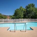 Inviting outdoor swimming pool with crystal-clear water, surrounded by lush greenery and a secure white fence, perfect for relaxation.