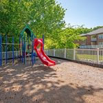 Inviting playground area with vibrant red slide and climbing structures, surrounded by lush greenery, perfect for family fun and relaxation.