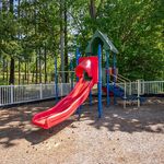 Charming playground with a vibrant red slide set amidst lush greenery, perfect for family-friendly outdoor fun.