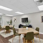 Modern communal dining area with stylish tables, chic green chairs, and decorative plants, perfect for gatherings and relaxing moments.