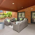 Inviting outdoor seating area with stylish wicker furniture and vibrant green cushions set against a warm brick backdrop.