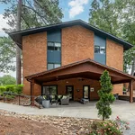 Charming brick apartment building set amidst lush greenery, featuring a cozy outdoor seating area under a stylish wooden awning.