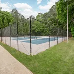 Inviting outdoor tennis court surrounded by lush green trees and clear blue skies, perfect for recreational activities.