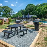 Inviting outdoor picnic area with a modern grill, adjacent to a sparkling pool surrounded by lush greenery.