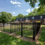 Charming townhouses with classic architecture surrounded by lush greenery and secure fencing under a bright blue sky.