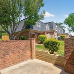 Charming townhouse exterior featuring classic brickwork, lush greenery, and a private fenced patio space.