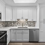 Modern kitchen with sleek white cabinetry, elegant stone backsplash, and stainless steel appliances.