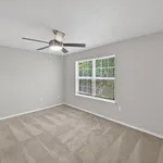 Bright bedroom with soft carpet, modern ceiling fan, and large window offering lush green views.