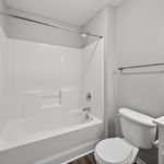 Modern bathroom with sleek white fixtures, a spacious bathtub, elegant tiling, and bright natural lighting.
