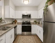 Modern kitchen with sleek stainless steel appliances, elegant white cabinetry, and a stylish granite countertop, enhanced by warm wooden flooring and decorative plants.