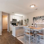 Modern kitchen and dining area with sleek white cabinetry, stainless steel appliances, and a cozy wooden dining set, perfect for entertaining.