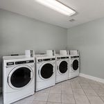 Modern laundry room with four sleek white washing machines set against a calming light grey wall, perfect for convenient living.