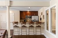 Chic apartment kitchen with modern stainless steel appliances, elegant wooden cabinetry, and a stylish breakfast bar with four high chairs.