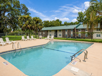 Inviting outdoor pool area with comfortable lounge chairs, surrounded by lush greenery and charming apartment buildings.