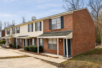 Charming townhouse exterior with classic brick facade, inviting front porch, and ample parking space in a peaceful neighborhood setting.
