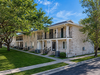 Charming brick apartment building with lush green lawn and elegant balconies, perfect for serene living.