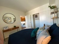 Sleep In, Stretch Out Charming bedroom with a modern aesthetic featuring cozy pillows, a sleek console table, and a welcoming mirror reflecting a glimpse into a bright kitchen area.