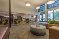 Gather. Relax. Unwind. Modern living space with high ceilings, stylish seating, and large windows offering plenty of natural light. Elegant kitchen and dining area in the background create a welcoming atmosphere.