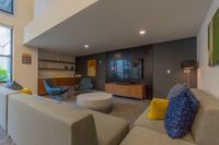 Where Neighbors Become Friends Modern living room featuring a sleek grey sectional sofa, vibrant accent pillows, wall-mounted TV, and stylish blue chairs with a chic coffee table.