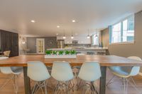 Host. Chill. Connect. Modern open-concept kitchen and dining area with stylish white chairs, wooden table, pendant lighting, and sleek stainless steel appliances.