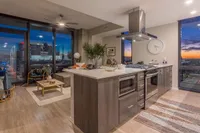 Chic modern apartment with open-concept kitchen, stylish living area, and expansive city views at sunset.