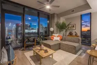Luxurious urban apartment living room with a breathtaking cityscape view, featuring modern furniture, vibrant decor, and floor-to-ceiling windows showcasing a stunning sunset.
