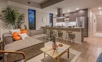 Modern open-concept living room and kitchen with stylish decor, featuring a cozy L-shaped sofa, elegant bar stools, and sleek stainless steel appliances.