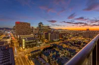 Breathtaking cityscape view from a high-rise apartment balcony, showcasing vibrant downtown lights against a stunning sunset sky.