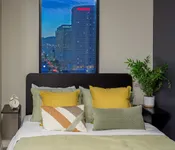 Chic bedroom featuring a cozy bed with colorful cushions, a modern potted plant, and a stunning city skyline view through the window.