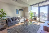 Bright and modern living room with a stylish gray sofa, contemporary armchair, and floor-to-ceiling windows providing stunning city views.