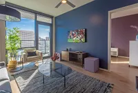 Bright, modern living room with stylish furniture, sleek TV setup, and expansive city views through large windows.