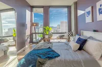 Bright and inviting bedroom with floor-to-ceiling windows offering stunning cityscape views, modern decor, and cozy bedding.