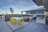 Modern rooftop terrace with vibrant yellow dining chairs, sleek white table, and cozy lounge area with outdoor TV and fire pit.