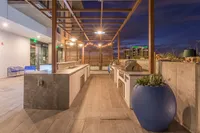 Chic outdoor kitchen with modern design, featuring sleek countertops, stainless steel grills, and ambient string lighting, perfect for evening entertainment against a cityscape backdrop.