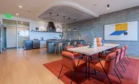 Elegant communal space featuring a modern kitchen with bar seating and a stylish dining area adorned with contemporary art and vibrant red chairs.