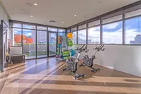 Modern and bright fitness room featuring exercise bikes and an array of colorful exercise equipment, with floor-to-ceiling windows offering stunning cityscape views.