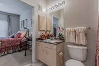 Elegant apartment bathroom with vanity, stylish decor, and a glimpse of a cozy bedroom featuring chic bedding.