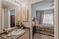 Modern apartment bathroom and bedroom view with elegant decor, featuring a granite countertop, stylish sink, lush potted plants, and a cozy, well-lit bedroom with chic curtains and a comfortable bed.