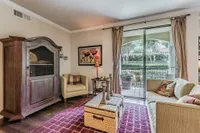 Cozy living room with elegant decor, featuring a plush couch, classic wooden cabinet, and a large window overlooking a serene garden patio.