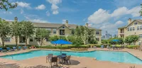 Beautiful apartment complex with a sparkling pool, surrounded by lush greenery and city skyline views.