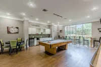 Chic recreation room featuring a stylish pool table, elegant seating, and a well-lit kitchenette, perfect for entertaining guests.
