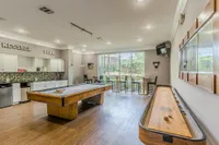 Spacious game room with pool and shuffleboard tables, stylish bar seating, and modern kitchen area.