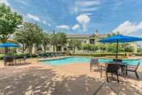 Charming apartment view showcasing a sparkling outdoor pool with stylish patio seating under vibrant blue umbrellas.