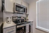 Sleek, Modern, and Functional Modern kitchen featuring sleek stainless steel appliances and stylish hexagon tile backsplash, enhanced by ample natural light from large window blinds.