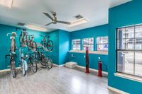 Indoor Bike Storage & Repair Station Modern bicycle storage room with vibrant teal walls, ceiling fan, and large windows, featuring multiple secure bike racks and convenient air pumps.