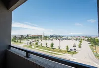 Fresh Air, Front Row Views Stunning balcony view featuring a lively commercial area with greenery, parking, and a beautiful horizon under a clear blue sky.
