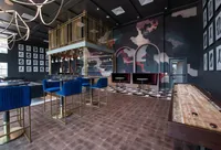 Chic and modern lounge area with elegant blue bar stools, stylish lighting, and a unique artistic wall design.
