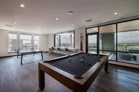 Chic recreational area featuring a modern pool table and ping pong setup, with panoramic views from large windows and a stylish balcony, perfect for entertainment and relaxation.